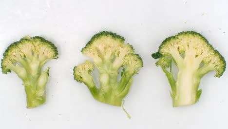 Water-splashes-in-slow-motion.-Top-view:-three-pieces-of-green-broccoli-washed-with-water-on-a-white-background